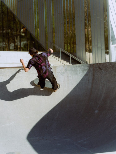 Photo of man skateboarding around a skatepark bowl. He is wearing Blinky Bills Shirt No. 1, a black over-sized, short-sleeved shirt with a print of pink and purple tattoo-designed tigers.